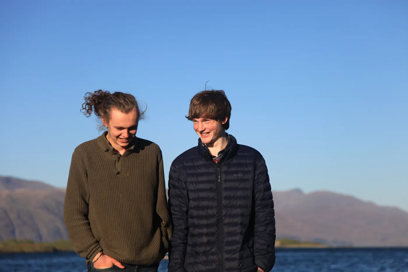 Roo and Neil laughing together beside a loch, with hills behind them