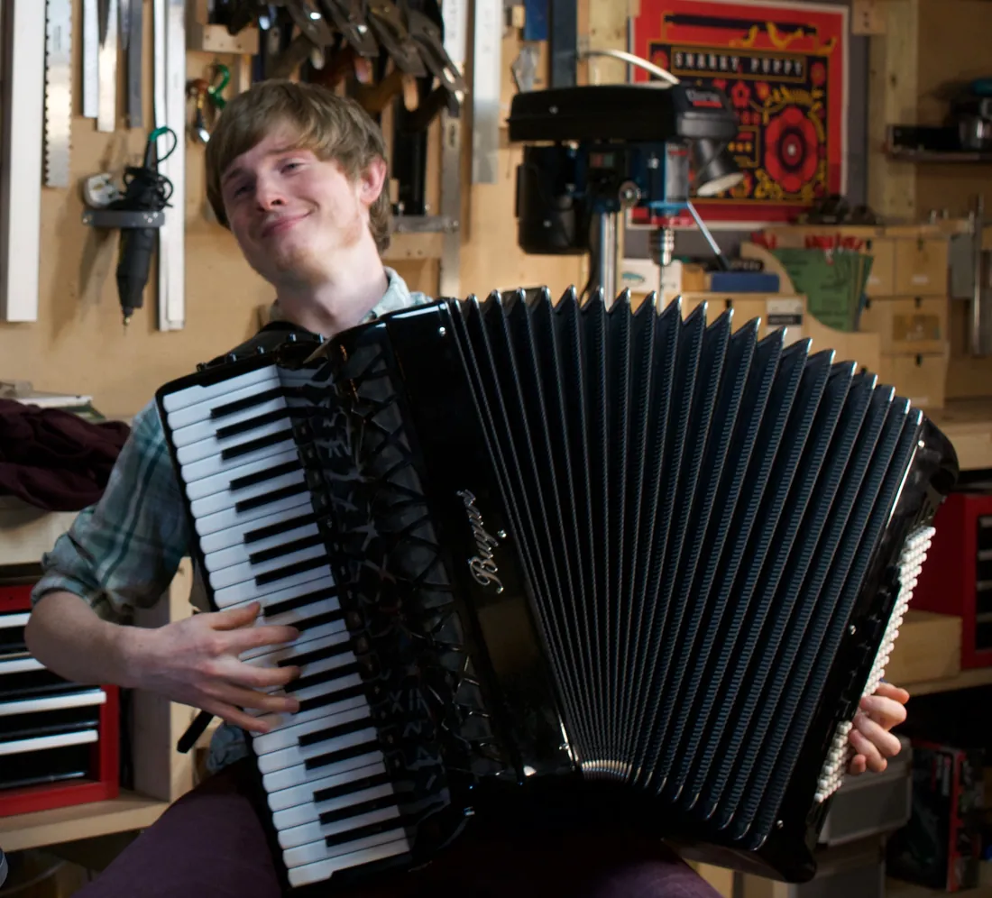 Neil smiling behind his black accordion in a workshop